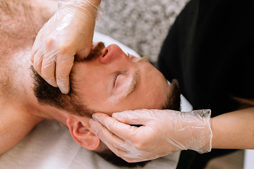 Man receiving facial buccal massage in beauty salon.Beauty and skincare concept with a beautiful woman. Middle aged male relaxed with massage for facial lifting